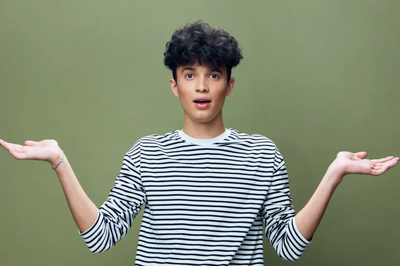 surprised man wearing striped shirt with raised hands against green background, expressing confusion and curiosity in studio lighting