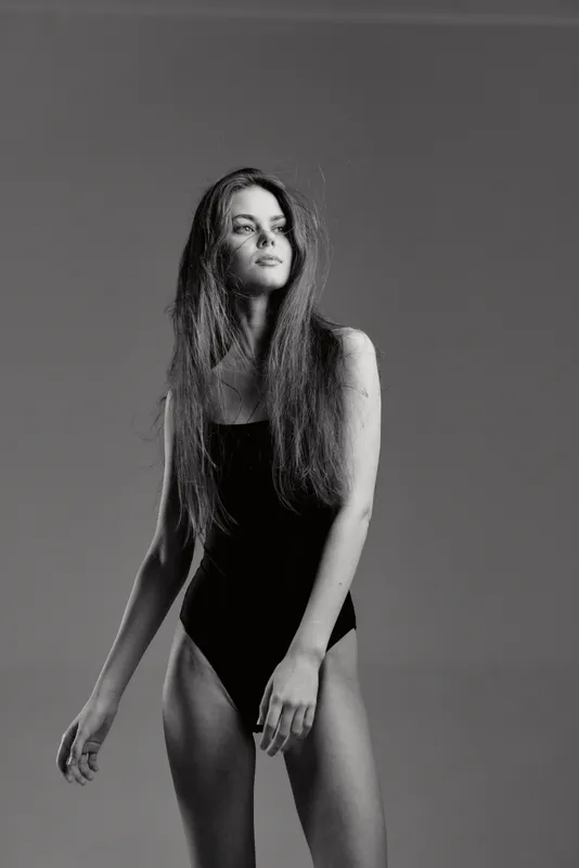 Black and white portrait of a young woman in a black swimsuit with long hair looking away, expressing calm and confidence.