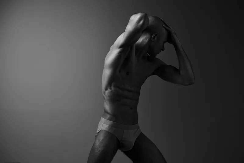 Black and white image of a man posing artistically, highlighting his muscular physique and dynamic movement. This striking composition evokes strength and emotion.