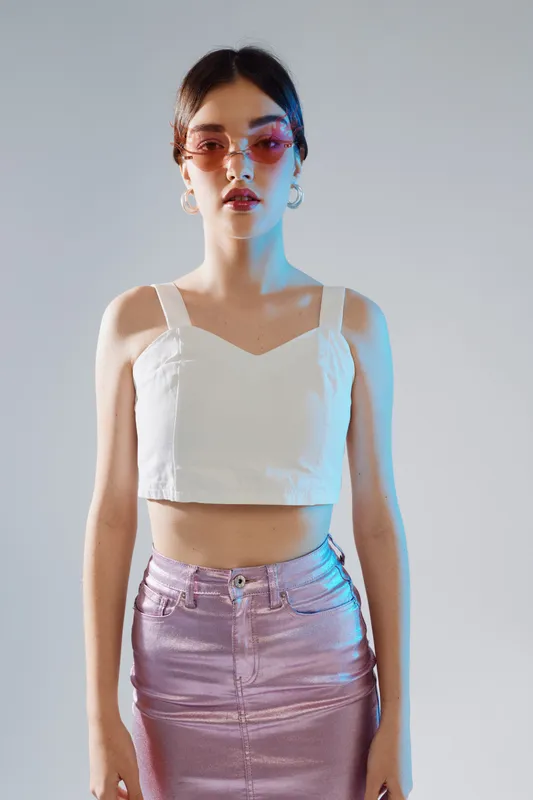Young woman beauty fashion model wearing pink sunglasses and metallic skirt poses confidently in studio with soft lighting on a neutral background.