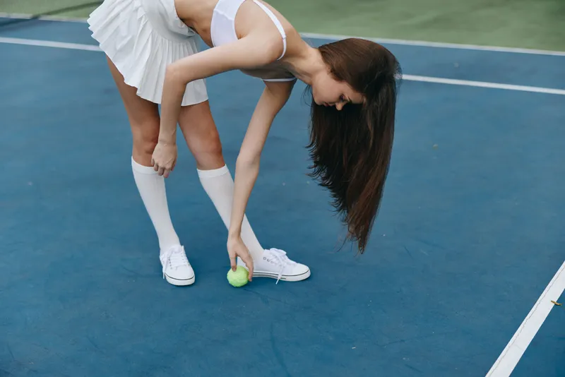 Young athletic woman preparing to serve on a tennis court, wearing a white tennis outfit, showcasing determination and focus in her expression