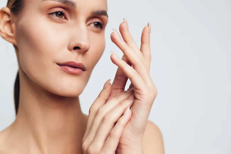 Young woman skincare face beauty hands touching spa close up portrait with soft natural skin glow on light background calm expression soft makeup clean composition