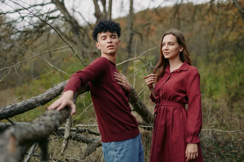 Young couple in an autumn forest captured in a genuine, natural moment; relaxed poses, warm tones and candid expressions convey a sincere connection and believable everyday romance and trust.