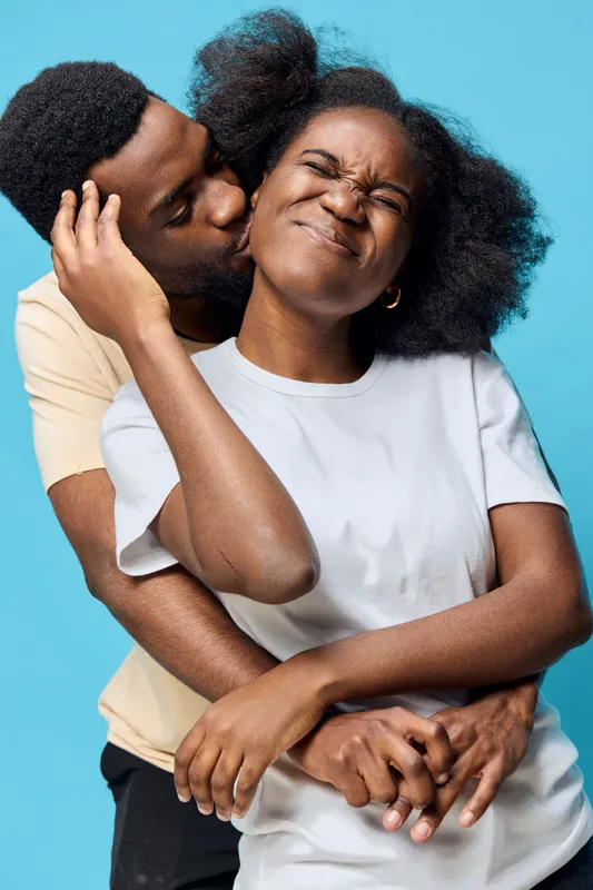 Happy couple enjoying an intimate moment together against a vibrant blue background, showcasing love, joy, and playful emotions in casual clothing