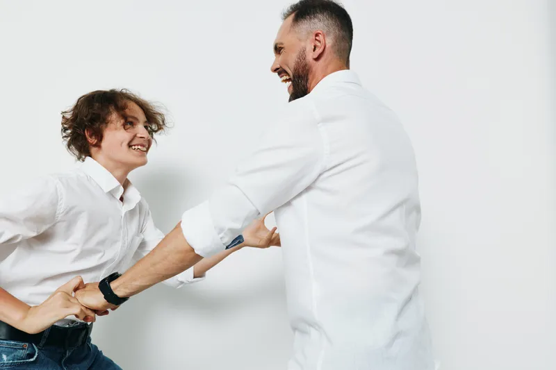 A professional man and colleague share a confident handshake in a bright studio. The moment shows positive emotions and professional energy against a solid color backdrop.