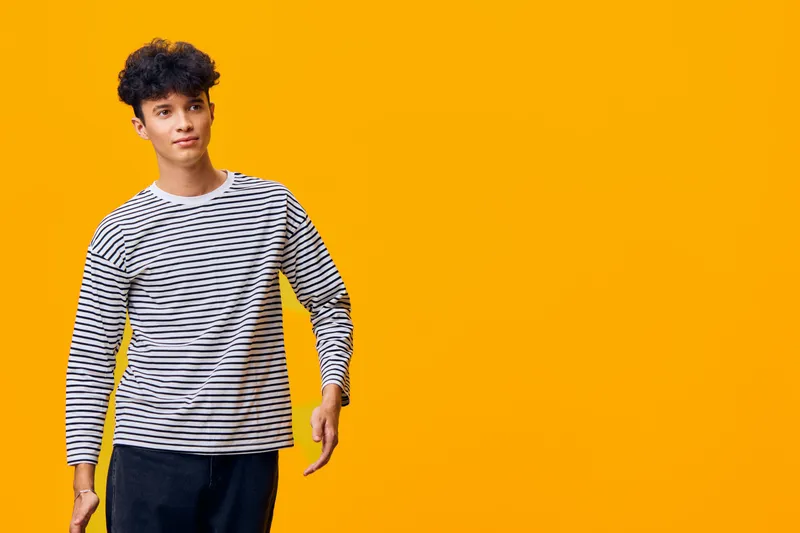 young man in striped shirt posing confidently against bright yellow background, casual style with curly hair and relaxed expression