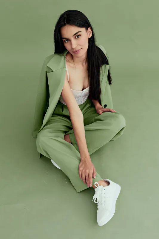 young woman in green suit sitting on floor, stylish casual wear, white sneakers, confident pose, minimalistic soft green background portrait