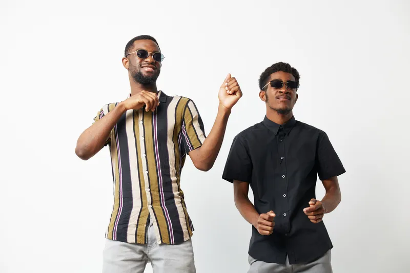 Two stylish black men dancing joyfully together in trendy outfits, radiating happiness and celebration in a bright and vibrant atmosphere.