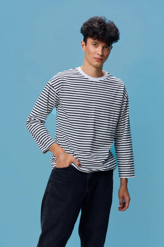 Young man in striped long sleeve shirt posing confidently against blue background with casual style and relaxed expression, showcasing modern fashion and youth culture.