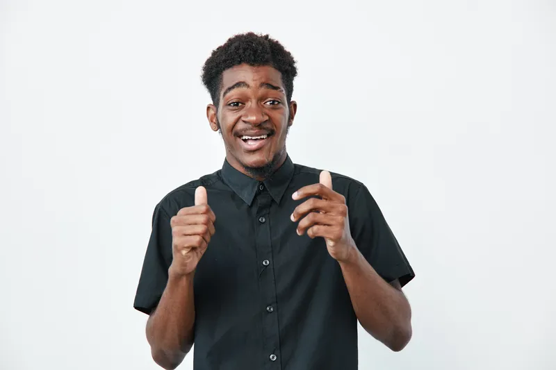 Young black man with dark skin wearing black shirt smiling and showing thumbs up gesture isolated on white background for positive emotion and approval.