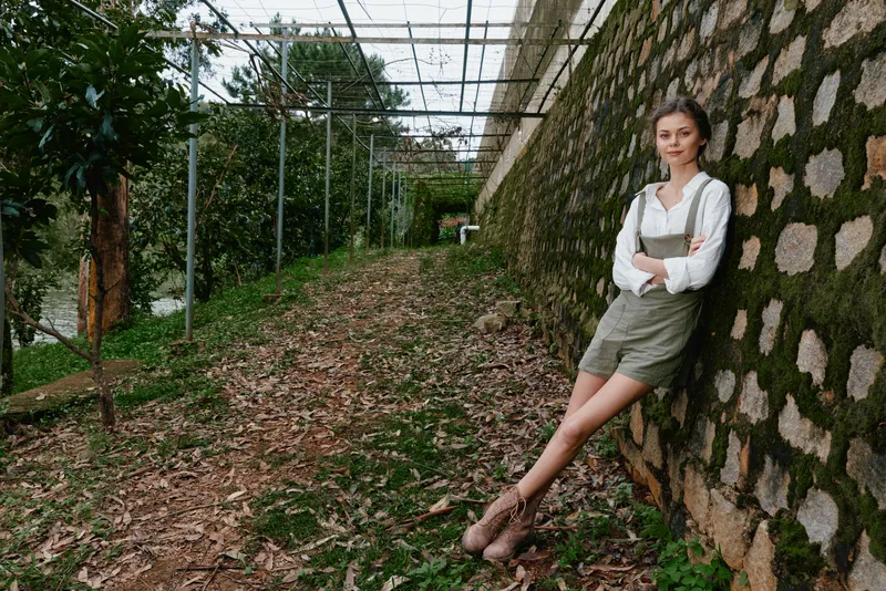 Young woman in casual outfit enjoying nature in the garden, showcasing a serene expression and a stylish look with a green backdrop