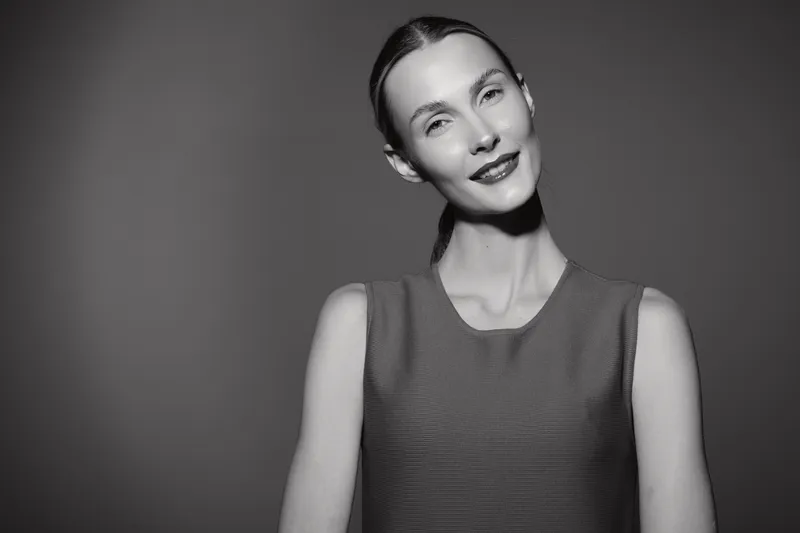 Slim white woman with fair skin and dark hair smiles gently in a studio portrait with soft lighting on a grey background. Concept for beauty and elegance.