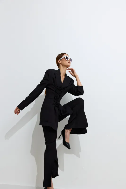 Fashion woman in black stylish outfit posing confidently against white background with sunglasses, showcasing modern minimalistic beauty and high fashion elegance.