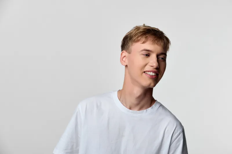 Man wearing a white t shirt with a bright smile stands against a neutral backdrop, conveying casual confidence and approachable mood for lifestyle, fashion, or wellness campaigns