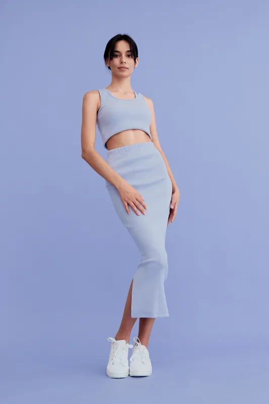 young woman wearing a casual blue ribbed outfit stands confidently against a matching blue background, showcasing modern fashion and minimalist style in full length.