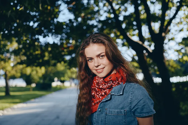 Lifestyle woman in modern boho-western denim street style with a red bandana, casual outdoor setting, and film color effect, smiling confidently in natural light.