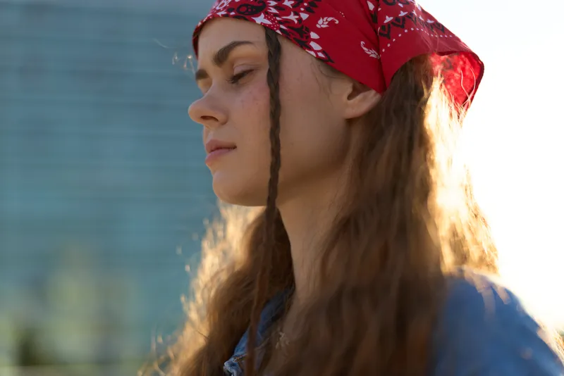 Lifestyle woman with modern boho-western denim street style wearing red bandana in soft natural light film color tones, casual outdoor fashion and serene expression