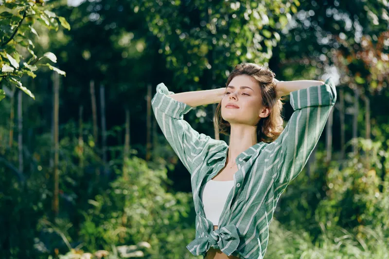 woman outdoors, relaxed, sunlit atmosphere with a calm smile, embracing nature, casual fashion, carefree mood, breeze in hair, peaceful landscape, fresh air, outdoor scene