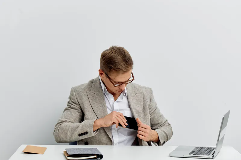 Professional young man in smart casual attire adjusting his shirt in a modern minimalist workspace desktop with laptop and notebook, demonstrating confidence and style. Business casual concept