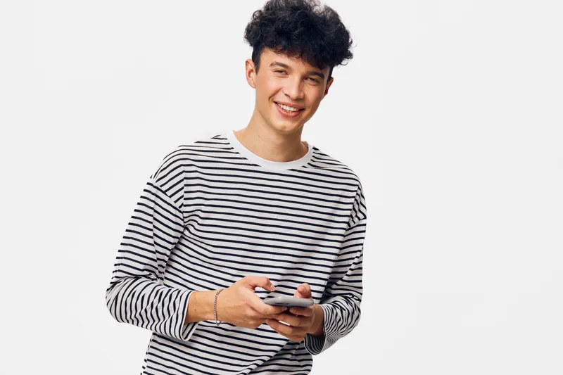 smiling man wearing striped shirt holding smartphone, casual style, curly hair, isolated on white background, cheerful young adult
