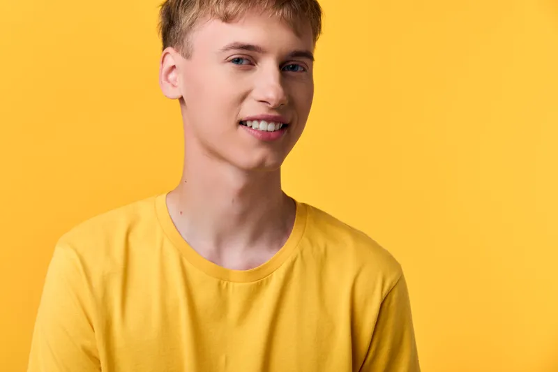 Smiling young man in a yellow tee against a vibrant yellow backdrop, relaxed studio style conveying optimism, warmth, and approachable fashion ideal for lifestyle campaigns