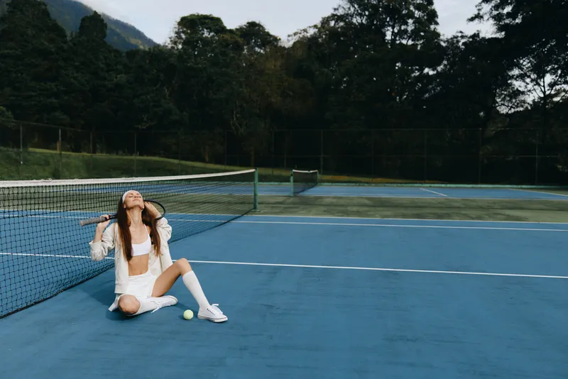Young female tennis player joyfully celebrating victory on the court, wearing a sporty outfit, with a lush green background, showcasing an energetic and vibrant atmosphere