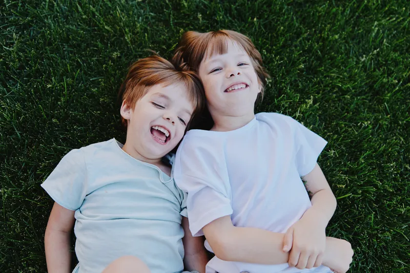 Happy children lying on grass, enjoying a sunny day, filled with laughter and joy. Their smiles capture the essence of childhood happiness and carefree moments.