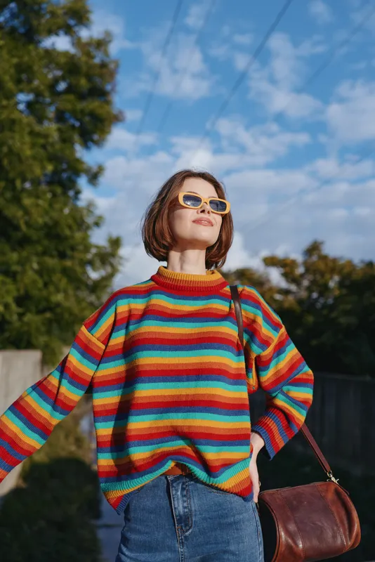 Woman in rainbow striped sweater wearing sunglasses and shoulder bag, outdoor portrait of confident young woman with short hair, casual fashion and sunny autumn mood.