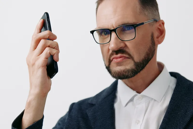 A confident business professional stands in a studio, holding a phone with a focused gaze. The isolated colored background highlights a strong, composed mood ideal for corporate messaging.
