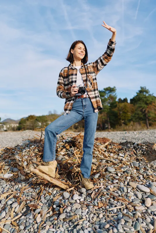 woman camera outdoor adventure travel landscape nature hiking posing joyful on rocky shore under blue sky with light breeze casual attire candid outdoor portrait capturing free spirit and scenic
