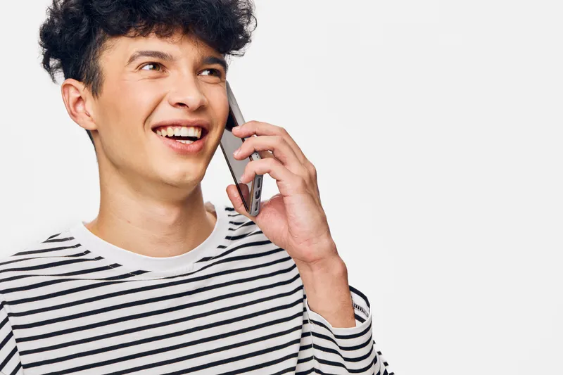smiling man talking on smartphone, casual striped shirt, curly hair, positive expression, isolated white background, young adult communication