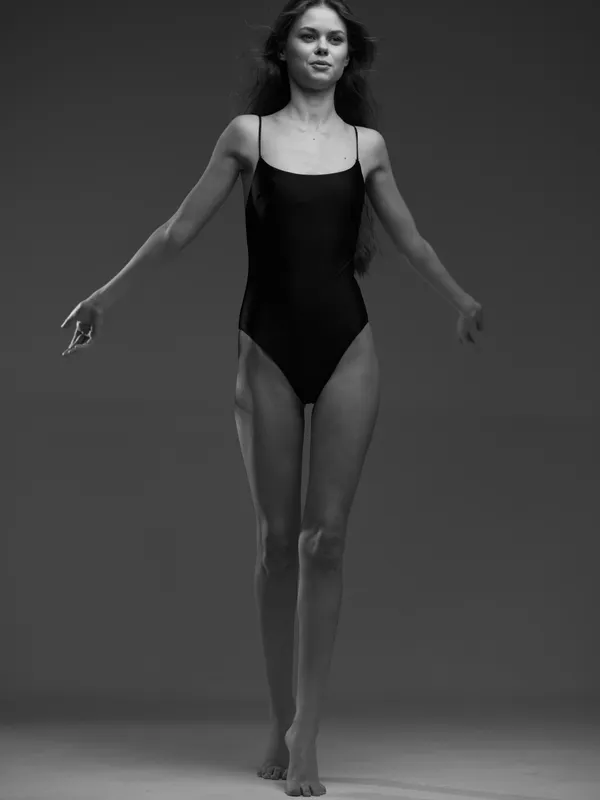 Black and white portrait of a slender woman in a black swimsuit with a neutral expression and graceful posture