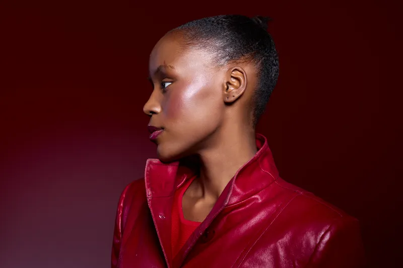 Profile of a young black woman with dark skin wearing a red leather jacket against a red background. Concept of fashion, beauty, and confident female portrait in studio lighting.