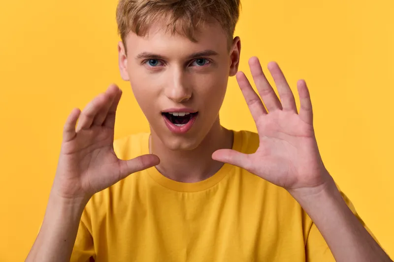 Young man with a surprised expression gestures with hands against a bright yellow background, casual tee, studio shot, capturing energy, movement and playful communication for lifestyle use