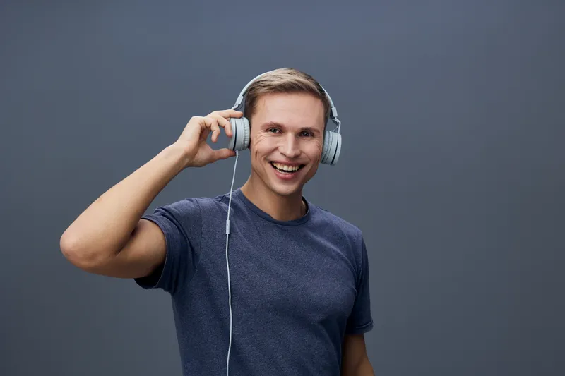 smiling man wearing headphones listen music enjoy audio entertainment casual dark t-shirt studio portrait isolated gray background digital detox concept