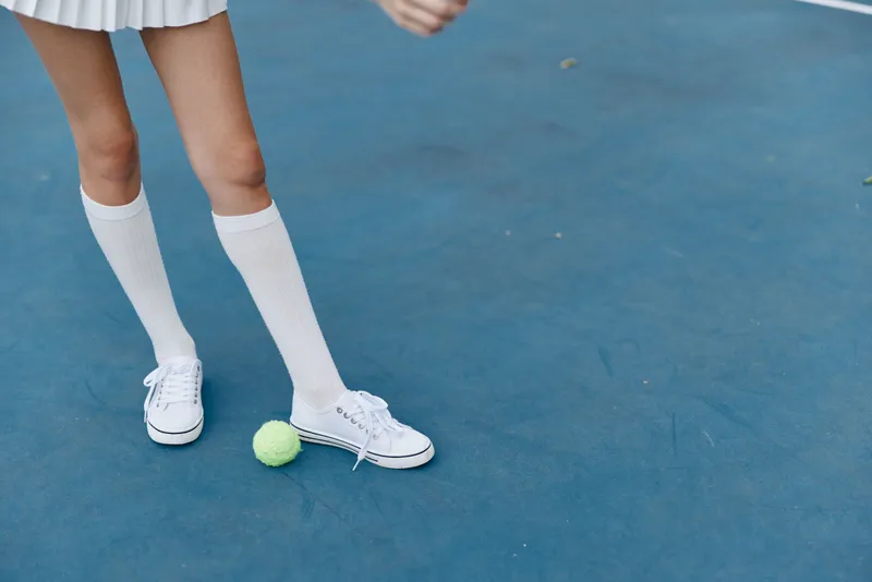 Young female athlete in a tennis outfit, demonstrating agility on a blue court with a tennis ball, exuding confidence and energy