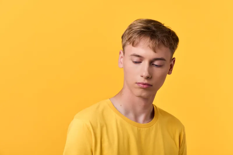 Young male in a yellow t shirt against a bright yellow backdrop, conveying calm, thoughtful mood with soft lighting for a minimalist studio look and modern fashion vibe