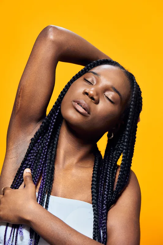 Beautiful young woman with braided hair poses against a vibrant yellow background, exuding calmness and confidence through her expressive emotions and stylish attire