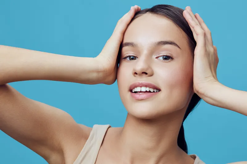 Young female model with a joyful expression against a blue background, emphasizing natural beauty and self confidence, wearing casual light clothing, vibrant colors and positive emotions