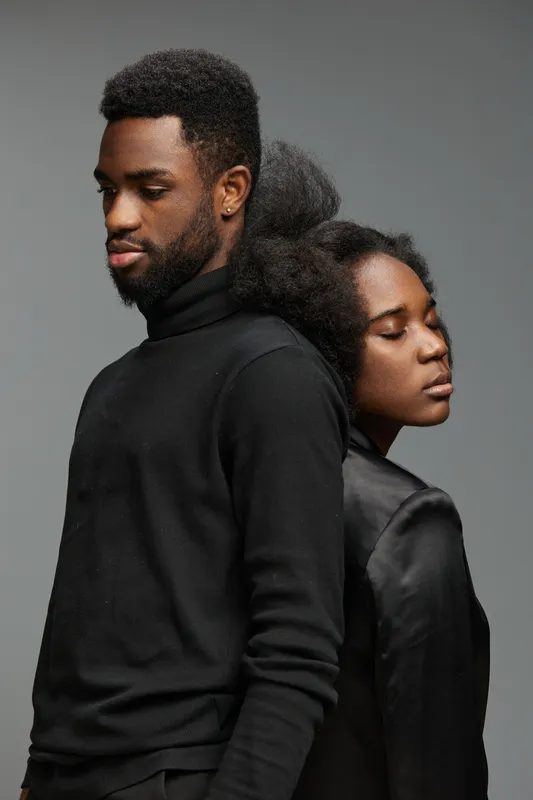 Portrait of a young Black couple dressed in stylish black attire, showcasing deep emotions against a neutral backdrop, perfect for conveying intimacy and connection