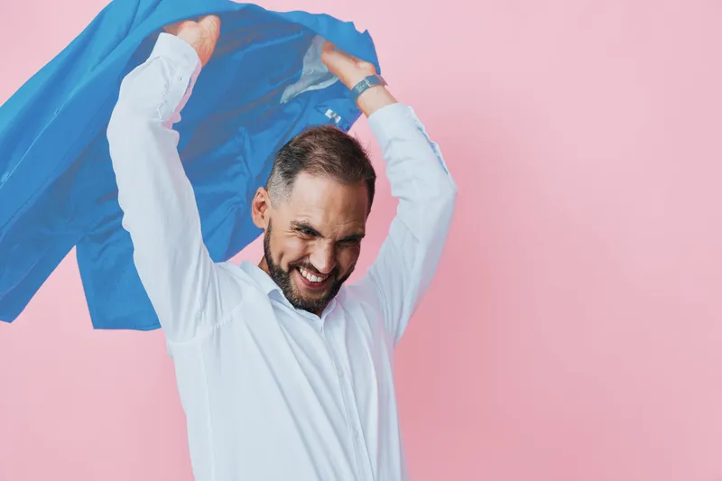 A confident business professional man celebrates success with a cape, posing against a vibrant colored backdrop, expressing joy, focus, and determination in a modern studio setting.