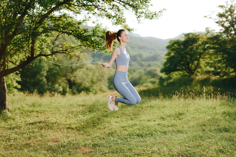 Fitness model jumping rope in a sunny green park wearing activewear, capturing joy and energy in a healthy lifestyle concept, emphasizing physical activity and wellness