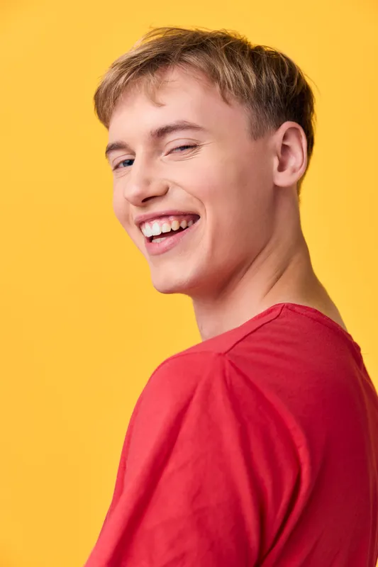 Smiling man in a red shirt stands against a bright yellow backdrop, a casual pose with a cheerful mood and warm lighting suited for lifestyle, fashion and positive energy visuals