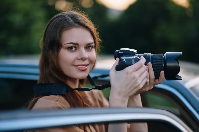 Young woman photographers smiling while holding a camera, showcasing passion, creativity, and outdoor exploration in a nature-inspired background.
