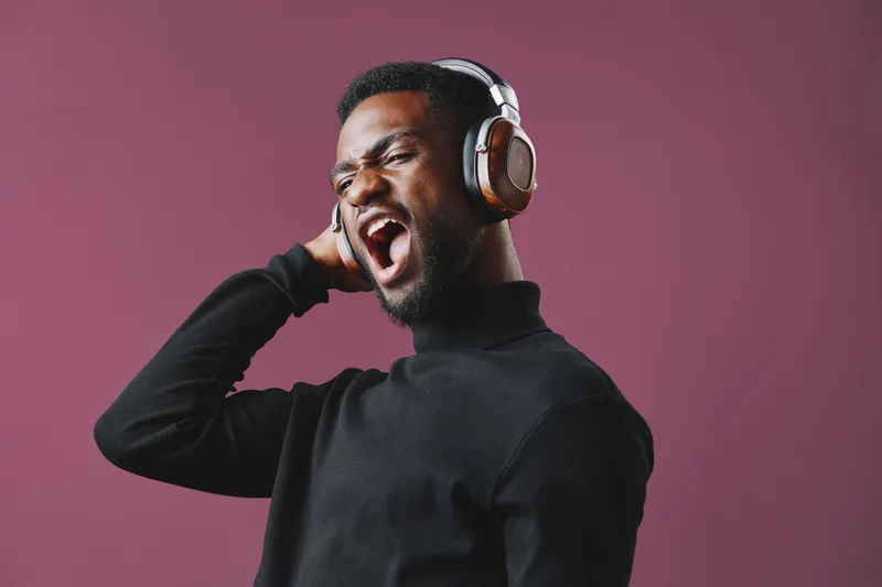 A joyful young Black man enjoying music with headphones, embracing a vibrant lifestyle and expressing emotions against a purple background