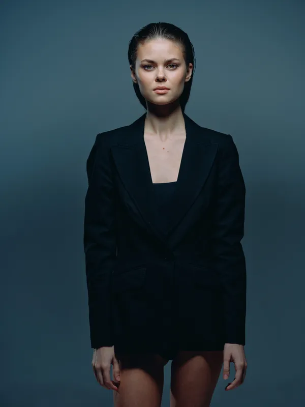 serious woman in black blazer with wet hair stands against dark background, expressing confidence and strength.