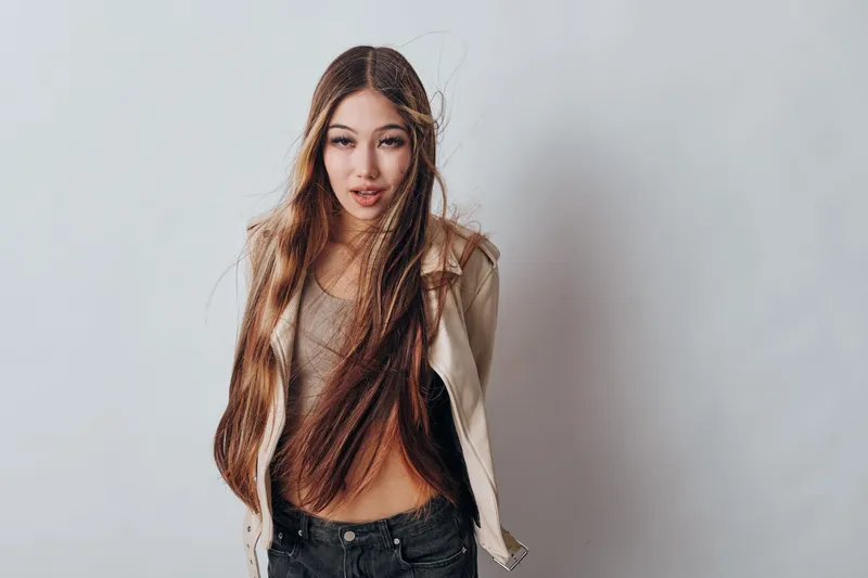 Young woman with long hair posing in casual beige jacket and top, looking confident against plain light background in studio. Beauty, fashion, model and hairstyle concept.