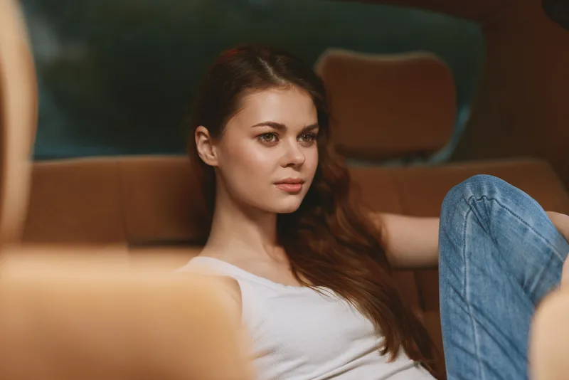 Young woman in casual attire relaxing in a car interior with a thoughtful expression, featuring warm tones and a cozy atmosphere.