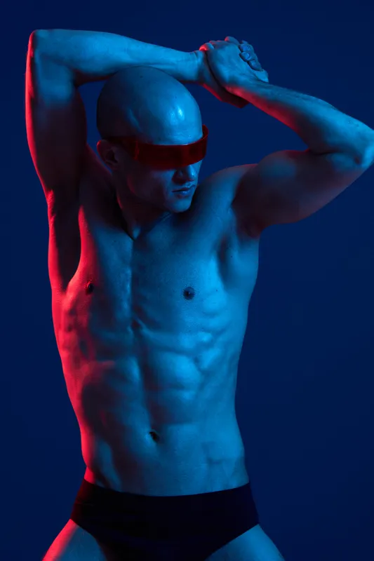 Athletic man posing dramatically with striking blue and red light, showcasing strength and vitality in a unique lighting setup. Perfect for fitness and fashion themes.