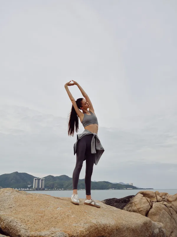 Inspirational young woman practicing yoga on a rocky beach at sunrise, wearing activewear and expressing tranquility and strength in a scenic coastal setting